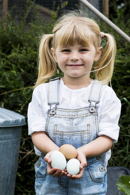 Блондинка стоїть у саду, тримає свіжі яйця, посміхається в камері.. — стокове фото