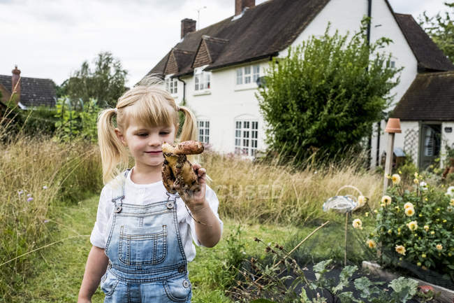 Blondes Mädchen steht im Garten und hält Kartoffelknödel in der Hand. — Stockfoto