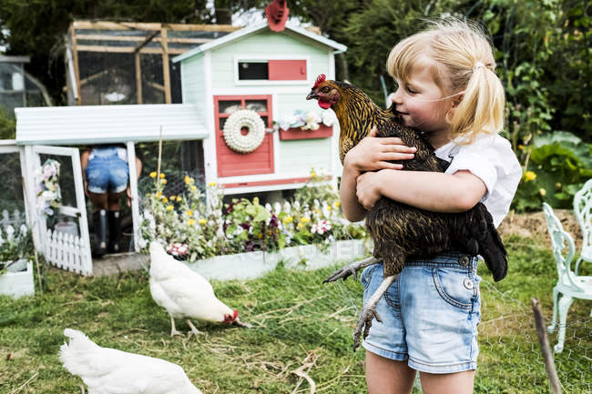 Блондинка, стоящая в саду перед курятником, держит коричневого цыпленка . — стоковое фото