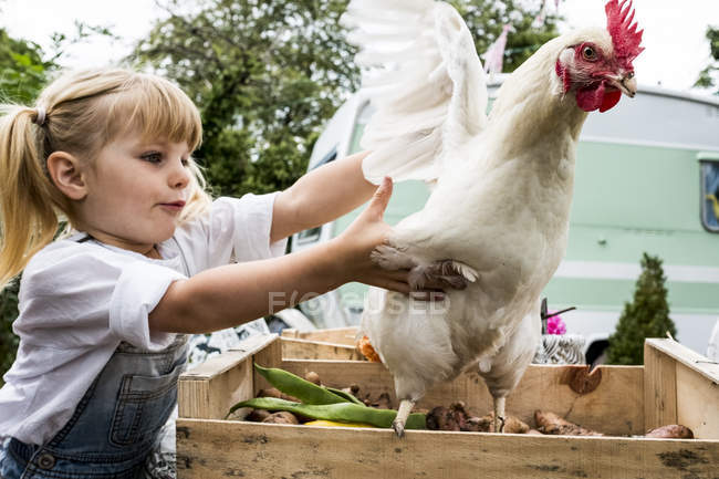 Close-up of blonde girl holding white chicken flapping wings. — Stock Photo