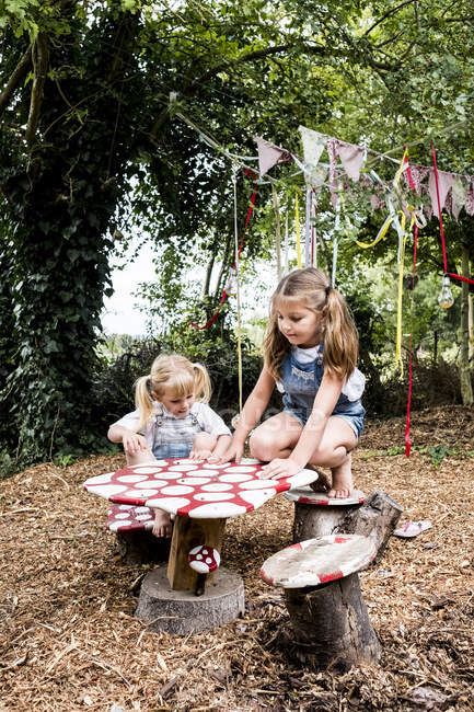 Duas meninas sentadas em uma pequena mesa de madeira no jardim e brincando . — Fotografia de Stock