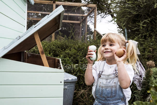 Menina sorridente de pé ao ar livre, segurando ovos recém-colocados nas mãos . — Fotografia de Stock