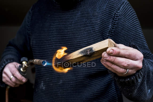 Close-up of man holding blowtorch, charring wooden handle of a knife. — Stock Photo