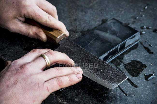 Großaufnahme der Hände einer Person, die ein handgeschärftes Messer auf einem Schleifstein schärft. — Stockfoto