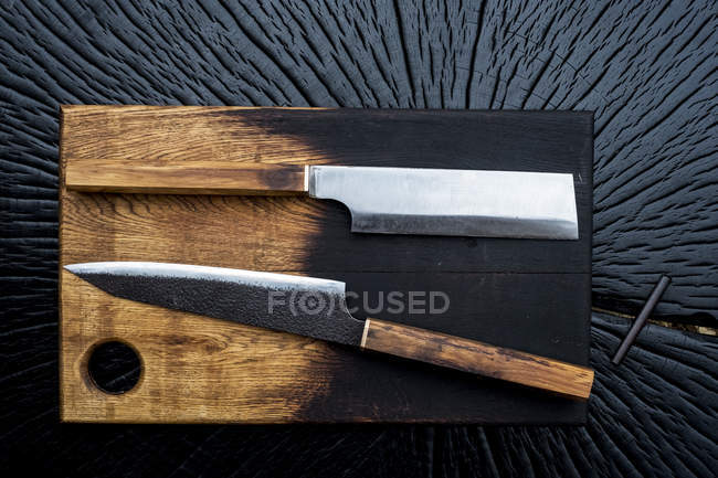 Primo piano ad angolo alto di due coltelli fatti a mano sul tagliere in legno . — Foto stock