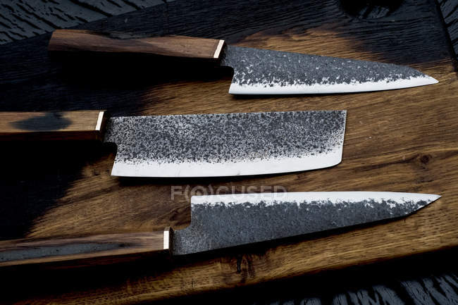 High angle close-up of three handmade knives on wooden cutting board. — Stock Photo
