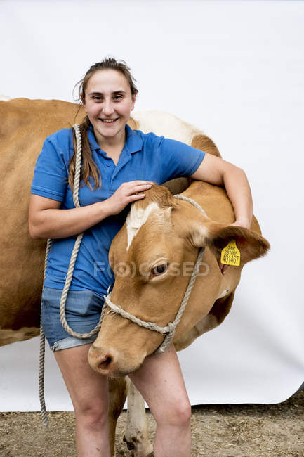 Porträt einer lächelnden Bäuerin, die eine Guernsey-Kuh umarmt. — Stockfoto