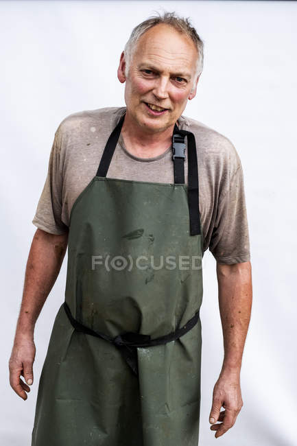 Retrato de un granjero vistiendo delantal verde sonriendo en cámara . - foto de stock