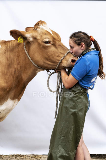 Portrait of female farmer wearing green apron hugging brown Guernsey cow. — Stock Photo