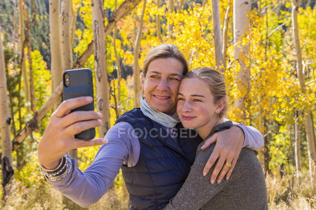 Ritratto di madre e figlia adolescente che scattano selfie con penne autunnali nel bosco — Foto stock
