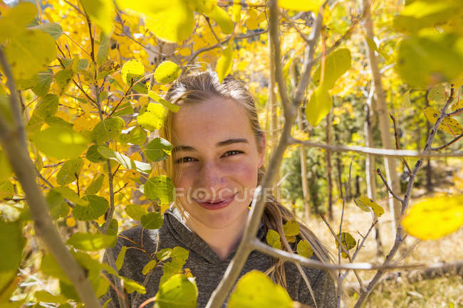 Portrait of smiling girl hiding behind autumn aspen leaves — Stock Photo