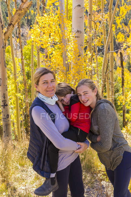 Madura madre con niño y niña posando en el bosque con árboles de álamo en el follaje de otoño - foto de stock
