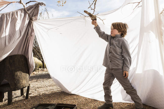 Мальчик младшего возраста играет с игрушкой в наружной палатке из простыней — стоковое фото