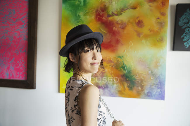 Japanese woman wearing hat standing in front of abstract paintings in an art gallery. — Stock Photo
