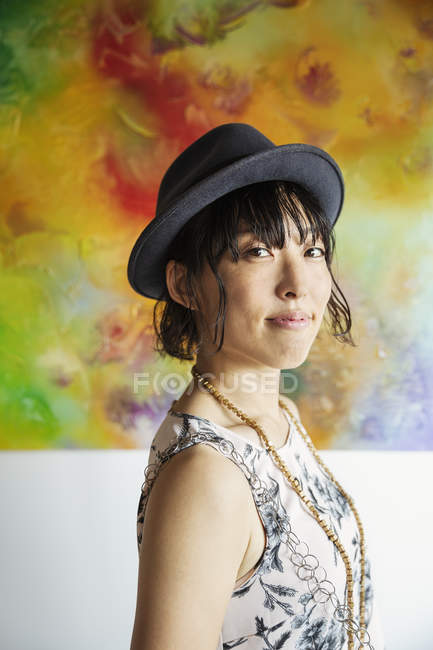 Японська жінка в капелюсі стоїть навпроти абстрактного живопису в художній галереї.. — стокове фото