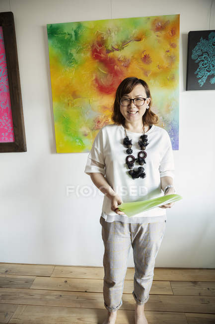 Mujer japonesa de pie frente a pinturas abstractas en una galería de arte, sonriendo en cámara . - foto de stock
