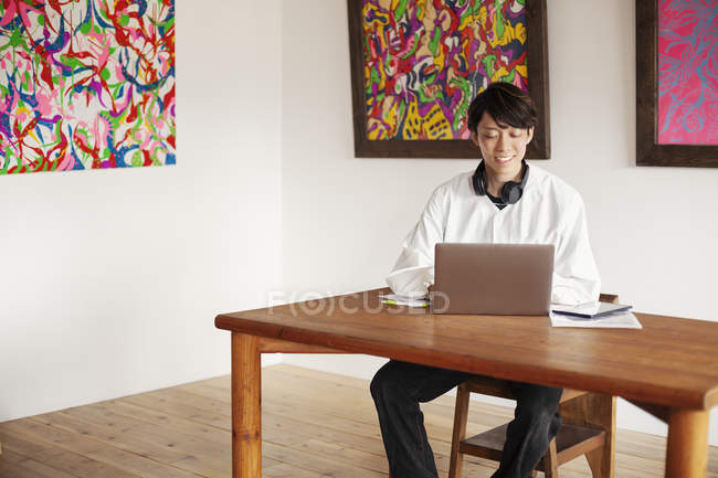Japaner sitzt an einem Tisch in einer Kunstgalerie und schaut auf Laptop-Computer. — Stockfoto