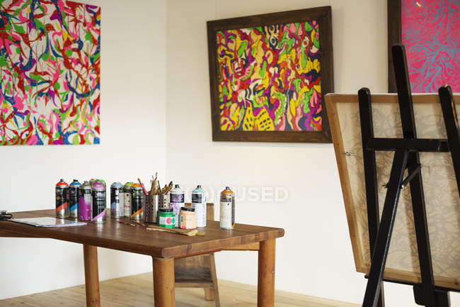 Interior view of art gallery with studio space, easel and cans of spray paint on a table. — Stock Photo