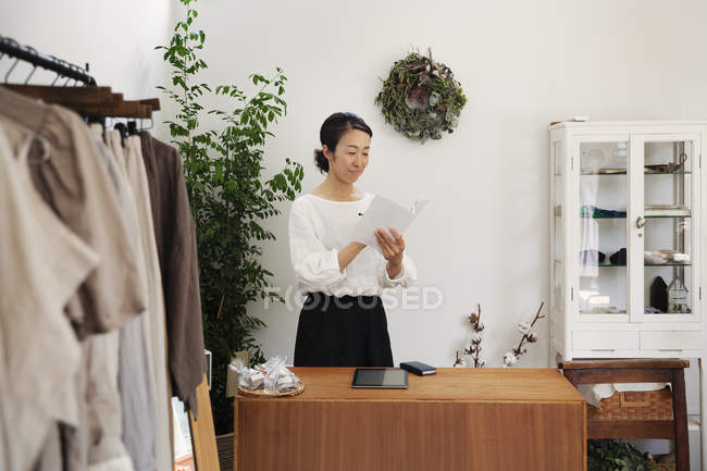 Japanese woman standing in a small fashion boutique, reading brochure. — Stock Photo