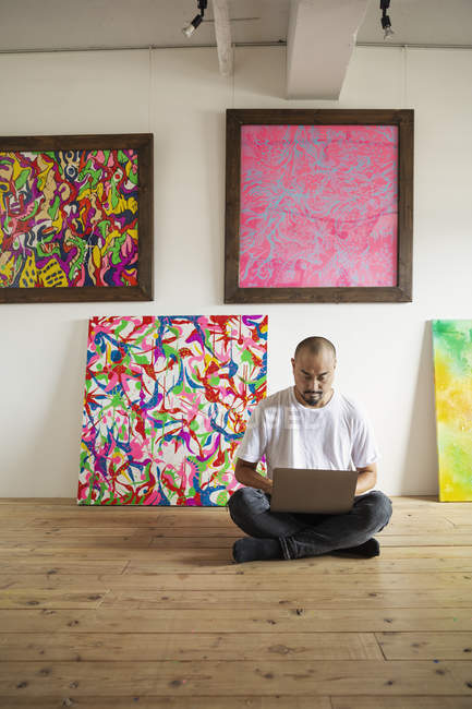 Японець сидить на підлозі художньої галереї і працює на ноутбуці.. — стокове фото