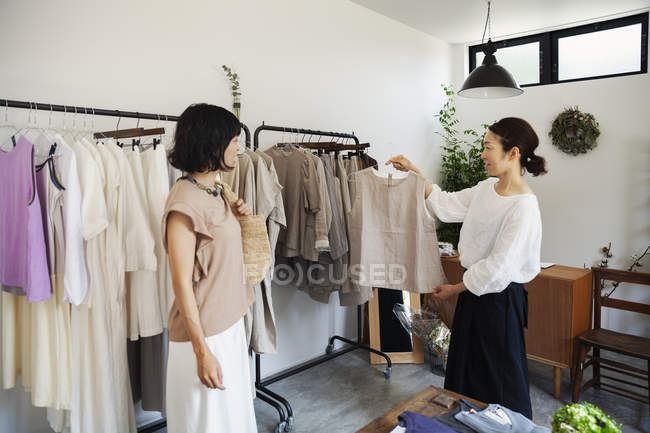 Two Japanese women standing in a small fashion boutique, looking at tops. — Stock Photo