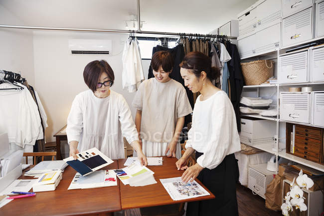 Three Japanese women standing at a table in a small fashion boutique, looking at fabric samples. — Stock Photo