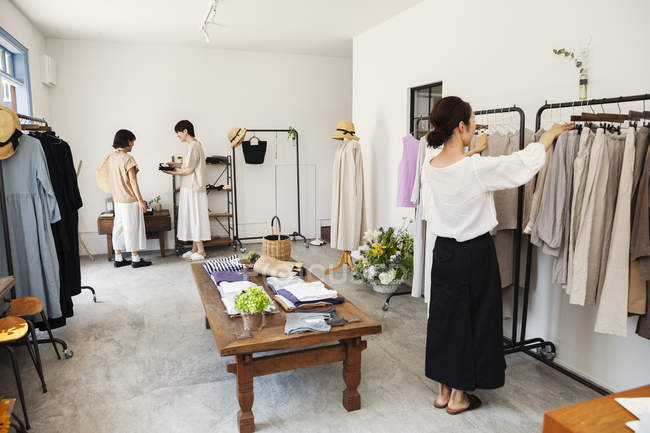 Três mulheres japonesas em pé em uma pequena boutique de moda, olhando para roupas em trilhos . — Fotografia de Stock