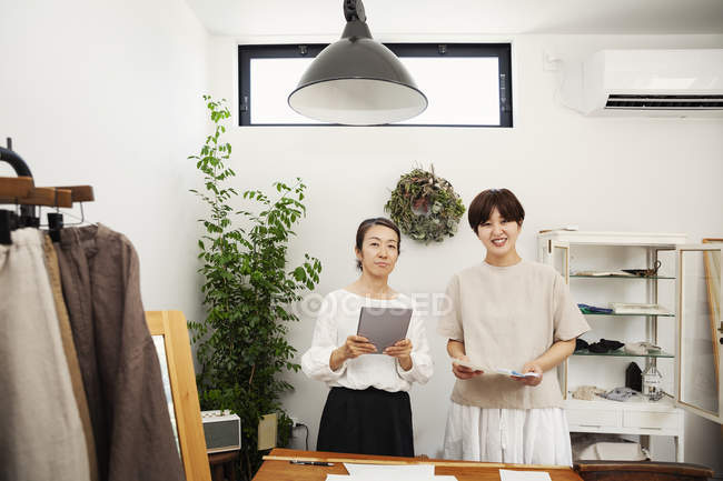 Dois lojistas japoneses em pé em uma pequena boutique de moda, segurando tablet digital, sorrindo na câmera
. — Fotografia de Stock