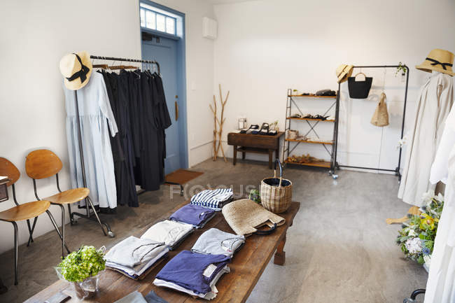 Vue intérieure d'une petite boutique de mode, avec des t-shirts sur une table basse et des robes sur des rails de vêtements . — Photo de stock