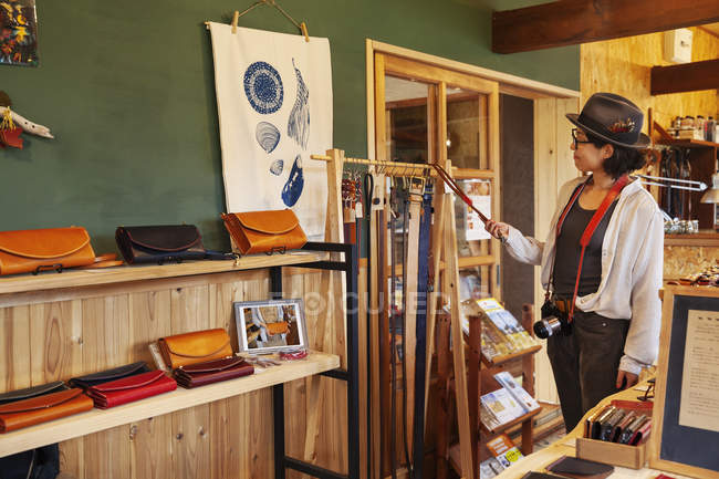 Japanese woman wearing hat and glasses browsing merchandise in a leather shop. — Stock Photo