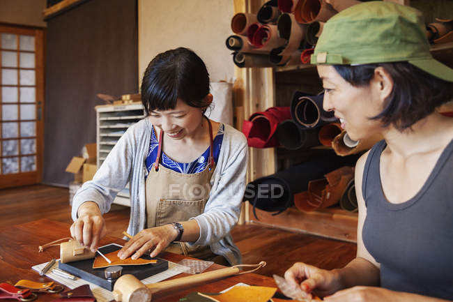 Two Japanese women sitting at a table, working in a leather shop. — Stock Photo