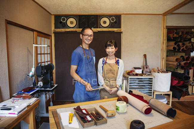 Японская женщина и мужчина в фартуках стоят в кожаном магазине и улыбаются в камеру
. — стоковое фото