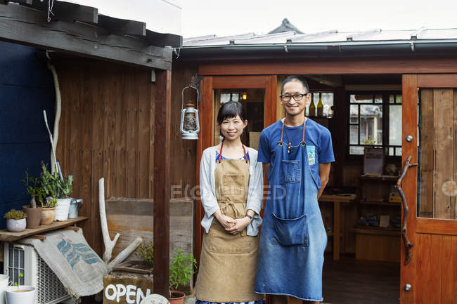 Japanese woman and man wearing aprons standing outside a leather shop, smiling in camera. — Stock Photo
