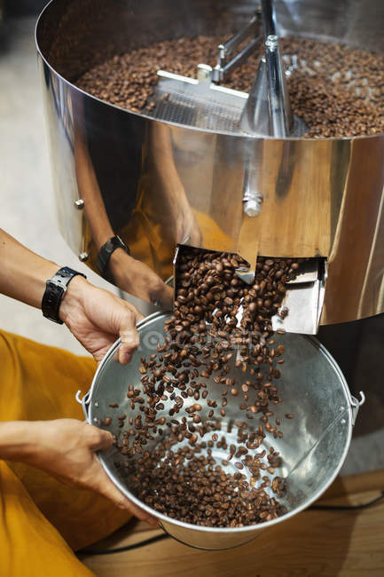 Alto ângulo close-up de pessoa segurando balde de metal com grãos de café recém-torrados . — Fotografia de Stock