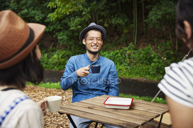 Japanese man and women sitting outdoors at a table, drinking coffee. — Stock Photo