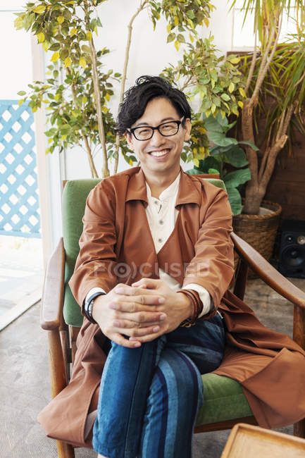 Männlicher japanischer Profi sitzt in einem Co-Working Space und lächelt in die Kamera. — Stockfoto