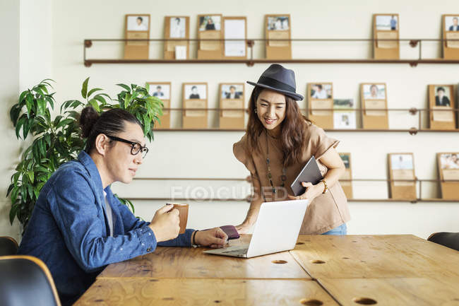 Male and female Japanese professionals at a table in a co-working space, using laptop computer. — Stock Photo