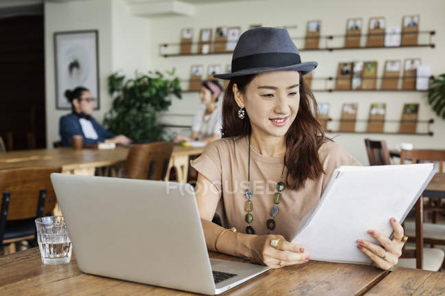 Japanese woman working on laptop in a co-working space, colleagues in background. — Stock Photo