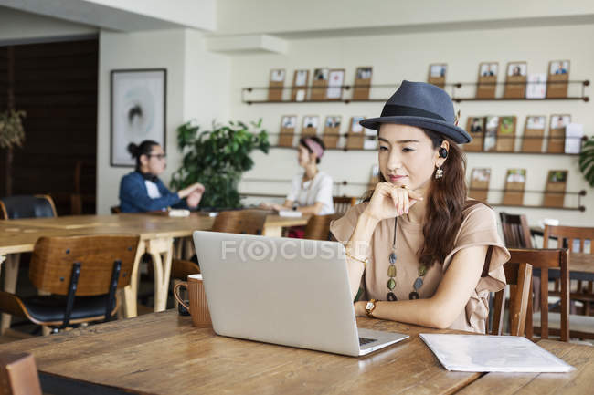 Femme japonaise travaillant sur un ordinateur portable dans un espace de co-travail, collègues en arrière-plan
. — Photo de stock