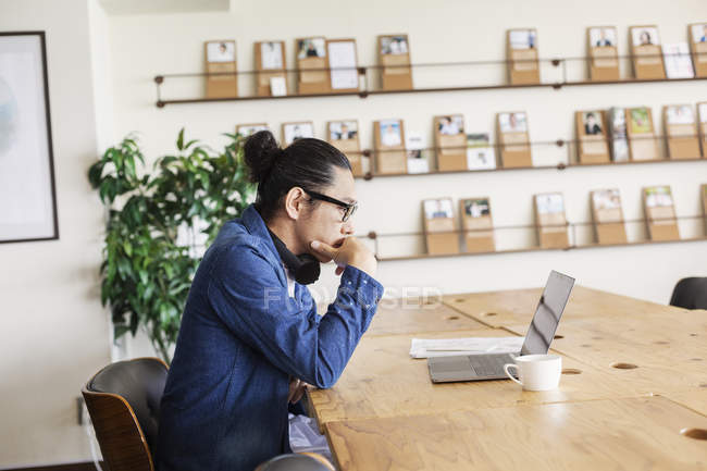 Male Japanese professional sitting at a table in a co-working space, using laptop computer. — Stock Photo