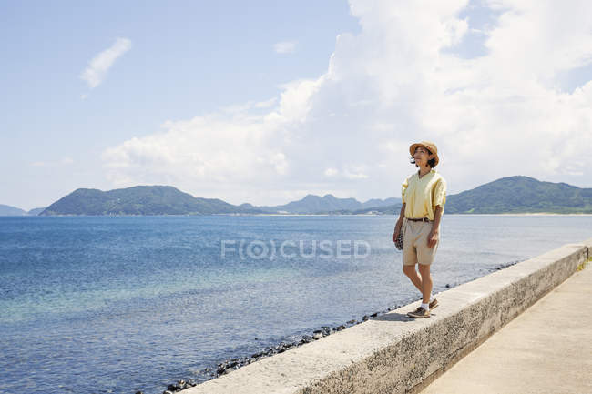 Japanerin mit Hut steht an einer Wand und blickt auf Ozean. — Stockfoto