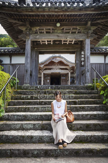 Japanerin sitzt auf Stufen vor einem buddhistischen Tempel. — Stockfoto