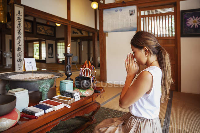 Japanese woman kneeling in Buddhist temple, praying. — Stock Photo
