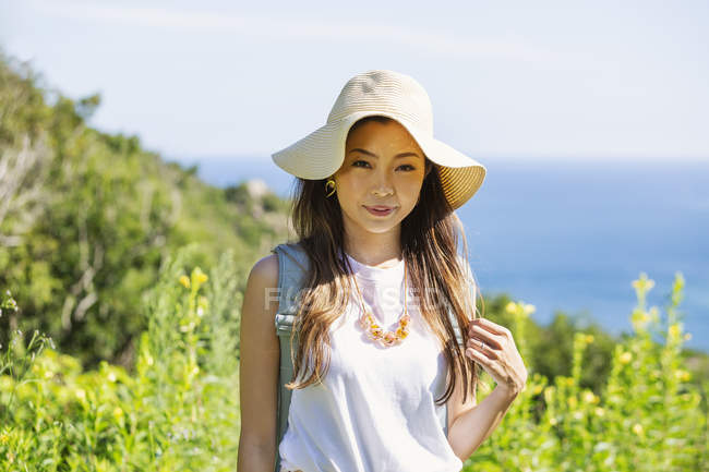 Japanese woman wearing hat standing on a cliff by ocean. — Stock Photo