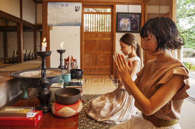 Two Japanese women kneeling in Buddhist temple, praying. — Stock Photo