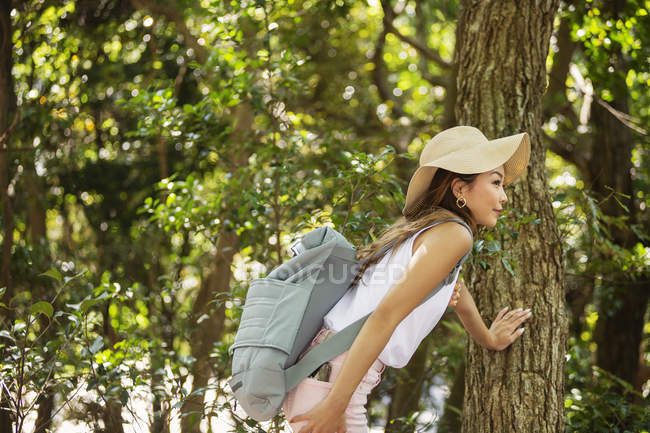 Japanerin mit Hut und Rucksack steht unter Bäumen. — Stockfoto