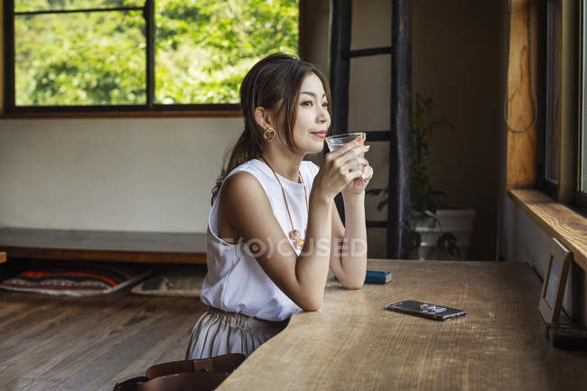 Lächelnde Japanerin sitzt an einem Tisch in einem japanischen Restaurant und trinkt. — Stockfoto