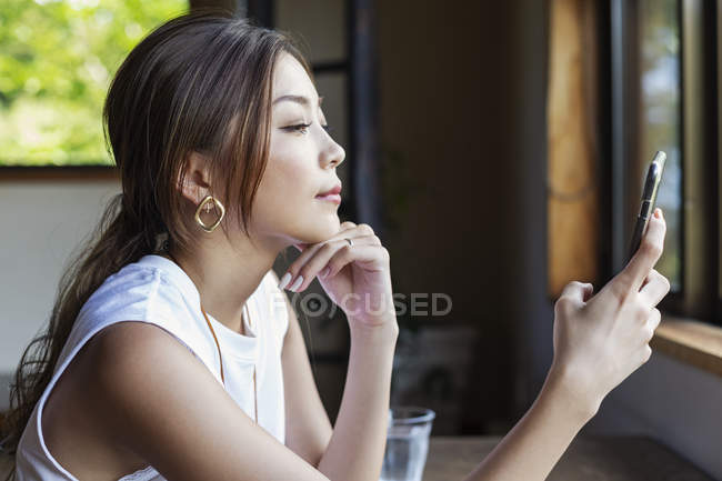 Mulher japonesa sentada em uma mesa em um restaurante japonês, usando telefone celular . — Fotografia de Stock