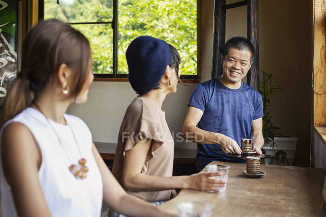 Camarero sirviendo a dos mujeres japonesas sentadas en una mesa en un restaurante japonés . - foto de stock