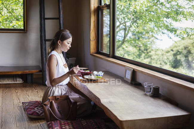 Mulher japonesa sentada em uma mesa em um restaurante japonês, comendo . — Fotografia de Stock